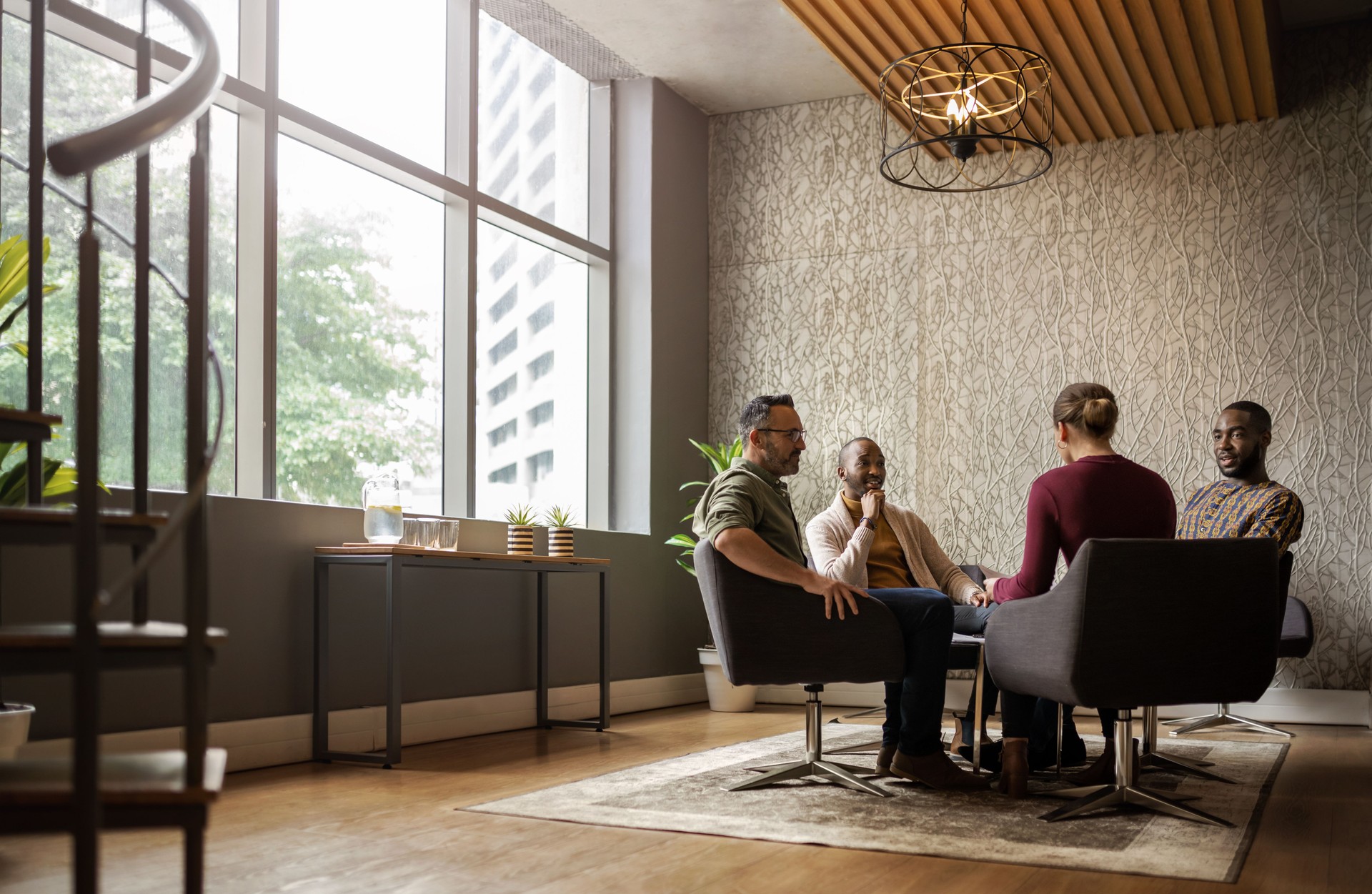 Wide shot of casual seated diverse business meeting in modern open workspace with large windows and sunlight shining in